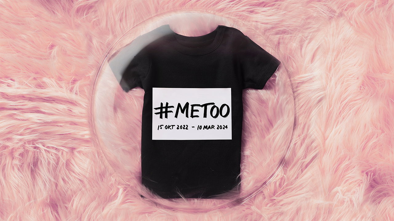 Foto på en svart t-shirt med vit ruta med texten #metoo. T-shirten ligger under en plastbubbla på en rosa matta.