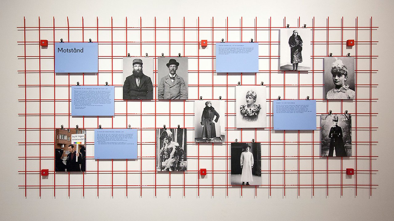 Pressphoto from the exhibition of a wall with a red grid with photos.